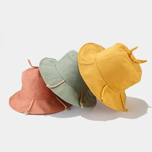 Minimalist cotton bucket hats in brick red, green, and yellow with top knot details