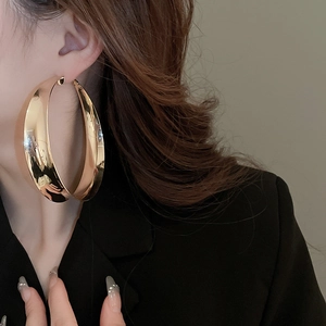 Close-up of a large gold hoop earring worn by a model with a black blazer and wavy hair