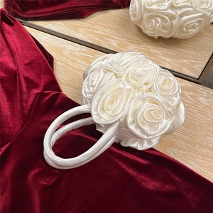 Close-up of handmade cream white satin rose flower evening bag on red velvet surface
