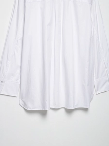 Detail view of the curved hemline and buttoned cuffs on a white long sleeve shirt