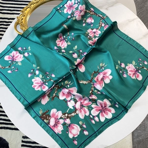 Elegant emerald green silk scarf with pink floral print displayed on a white table
