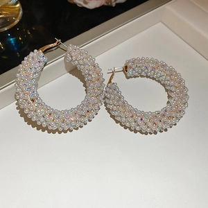 Detail view of large C-shaped gold hoop earrings with white pearls and clear diamonds