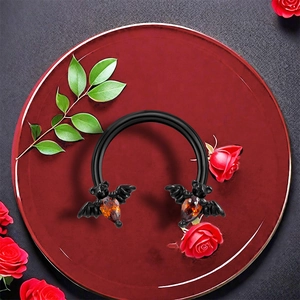 Close-up of black bat horseshoe ring with amber zircon set on red roses and green leaves
