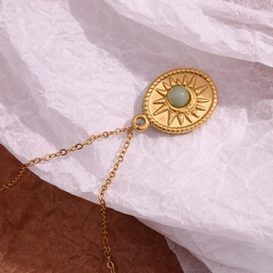 Macro shot of an 18K gold-plated oval sunburst pendant with a green gemstone inlay