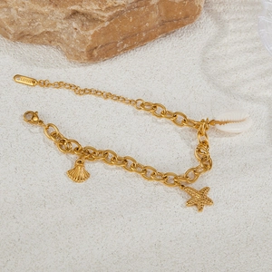 Detail of golden stainless steel bracelet with starfish and seashell charms on white sand