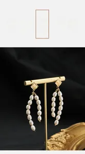 Detail of freshwater pearl drop earrings with golden geometric studs on black velvet