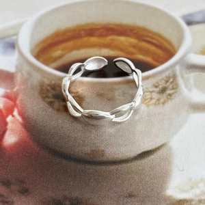 Polished silver irregular wave open ring placed on a coffee cup edge lifestyle shot