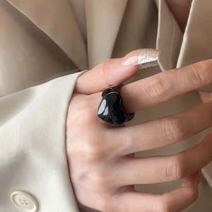 Close-up of black resin heart ring on finger with warm beige blazer background