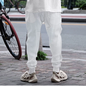 Close-up of men's white knit trousers featuring detailed cable knit patterns on fabric