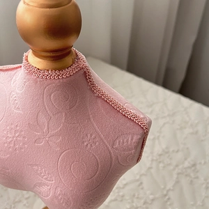 Close-up of pink embossed fabric jewelry display with gold finial and woven trim