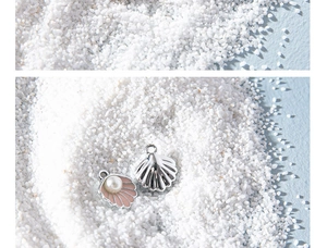 Macro detail of shell-shaped pendants with pink enamel and white pearl on sand
