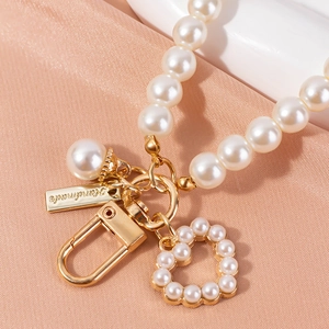 Elegant pearl keychain with heart charm and golden lobster clasp on peach silk background
