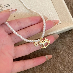 Elegant pearl necklace featuring a golden rocking horse and coin pendant held in hand