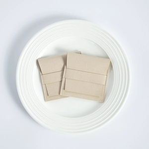 Detail of two beige microfiber jewelry pouches with flap closure on a white plate