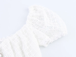Detail of white lace dress showing off-shoulder puff sleeve with elastic cuffs