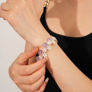 Detailaufnahme eines Blumen-Emaille-Armbands mit violetten und rosa Blüten am Handgelenk