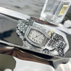 Macro shot of a silver tonneau watch with rhinestone bezel on a reflective metal tray