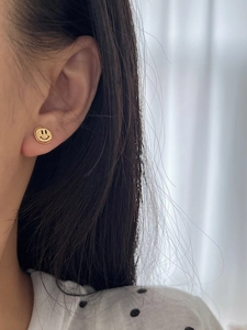 Gros plan d'un mannequin portant de petites puces d'oreilles smiley dorées en argent