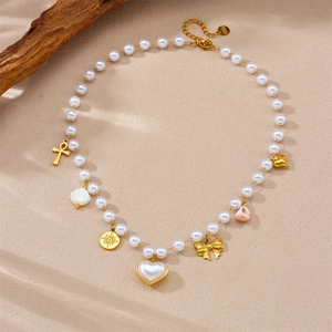 Elegant pearl chain necklace with gold heart shell and bow pendants on a textured surface