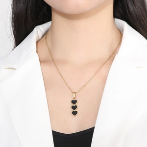 Close-up of three black heart pendants on a gold chain worn with a white blazer