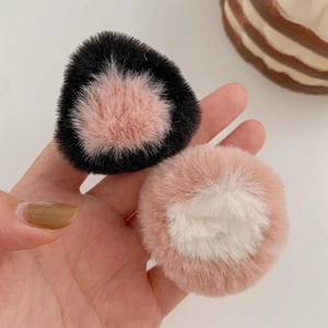 Detail view of plush faux fur ear hair clips in pink and black held by hand
