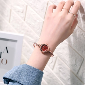 Close-up of rose gold bangle watch with red starry dial and woven steel cable strap on wrist