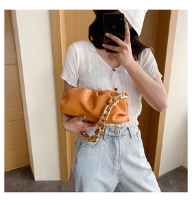 Close-up of bright orange dumpling bag featuring soft pleated leather and bold gold chain