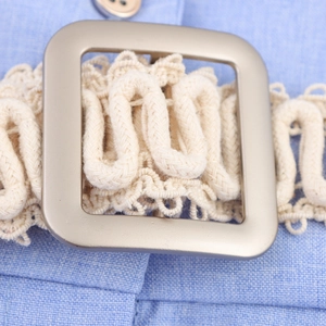 Detail van een beige gevlochten riem met gesp op een mouwloze blauwe linnenlook jurk