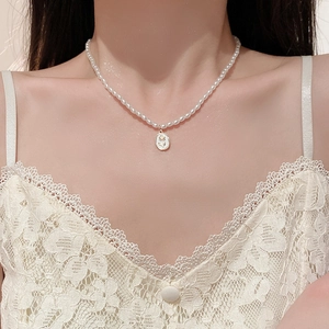 Détail d'un collier de perles avec pendentif ovale orné d'une rose dorée en relief