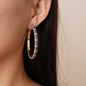 Detail of large hoop earring with brown plaid fabric finish and golden metal inner lining