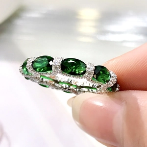 Close-up of a silver ring featuring oval green gemstones and small diamond accents