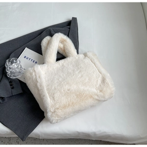 Detailed overhead shot of a cream plush tote bag on white fabric with fashion accessories