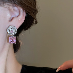 Detail of flower-shaped earrings with pink square stones and zircon inlays on model