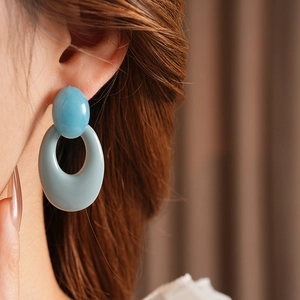 Close-up of light blue oval resin hoop earrings worn by a model for a vintage look
