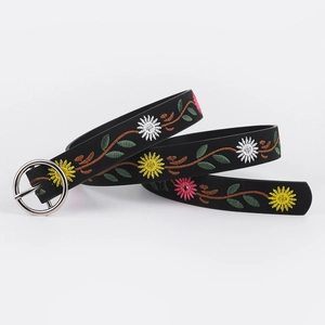 Detail view of colorful floral embroidery and round silver metal buckle on a black leather belt
