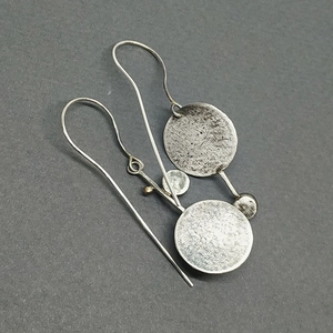 Artistic round metal drop earrings with silver finish and brushed texture on grey background