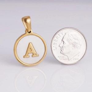 Macro detail of gold stainless steel round letter A pendant next to a size reference coin