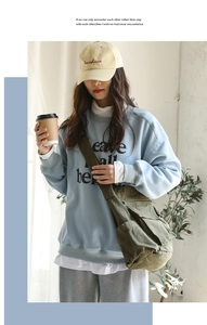 Close-up of olive green canvas messenger bag paired with blue sweatshirt and beige cap