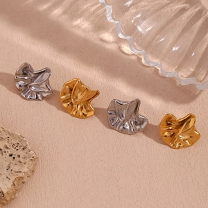 Detailed view of gold and silver irregular pleated stud earrings on a textured background