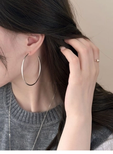 Close-up of large silver C-shaped hoop earrings worn by a model for a minimalist look