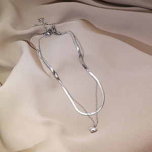 Close-up of a double-layered silver necklace with a heart pendant on silk fabric