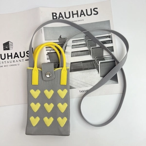 Detailed knit grey phone bag with yellow hearts and strap on a minimalist book background