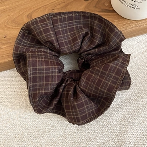 Detailed view of a brown plaid fabric scrunchie styled on a rustic wooden tray