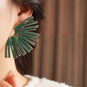Macro close-up of a model wearing large fan-shaped gold earrings with green rhinestones