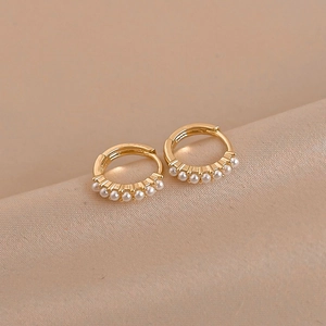 Macro shot of minimalist gold hoop earrings with small white pearls on champagne silk