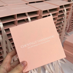 Caja rosa para joyas con textura de papel y tirador de cinta con logo dorado