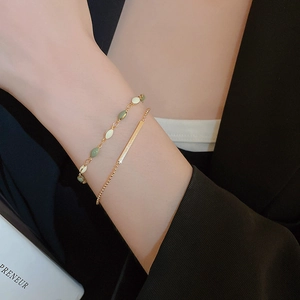 Close-up of gold double-layer bracelet with green leaf beads and minimal metal bars