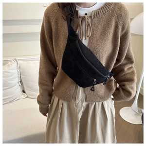 Detail of black corduroy belt bag worn as a crossbody chest pack in a cozy home setting