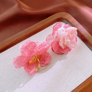 Detailed view of handmade pink lace flower clip-on earrings on a rustic tray