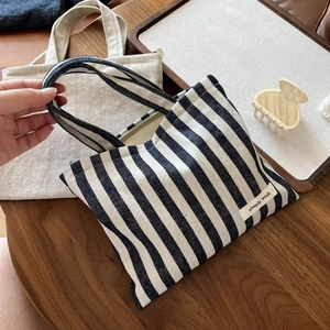 Minimalist black and white striped canvas tote bag with top zipper on a wooden table